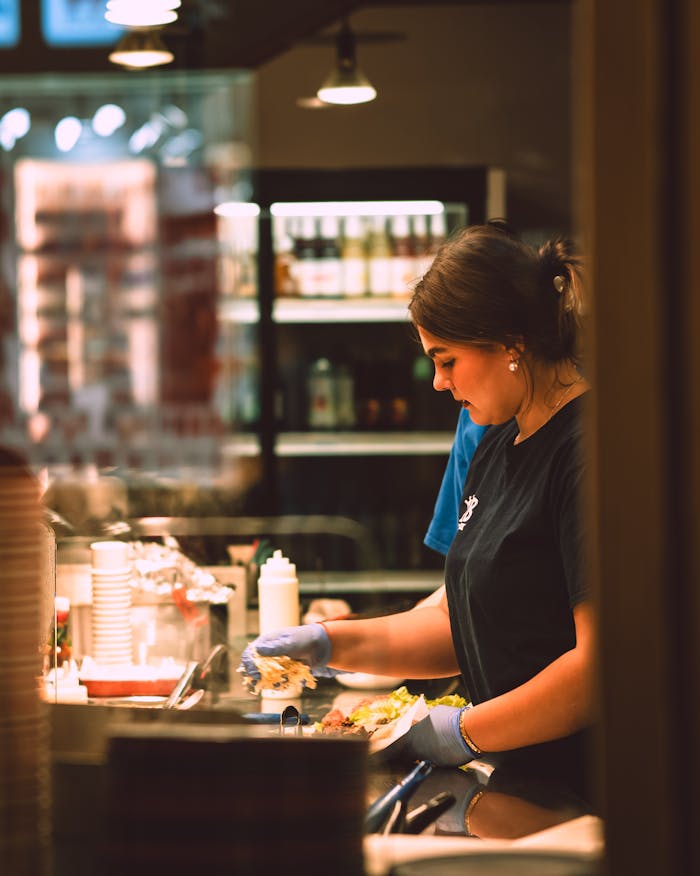 about-us-01 A focused moment of a young woman preparing food in a busy kitchen setting.